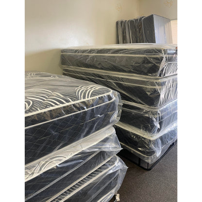 Vivians 13" Innerspring Mattress With Black Quilt, Inside Of A Showroom, Stacked On Top Of Other Mattresses