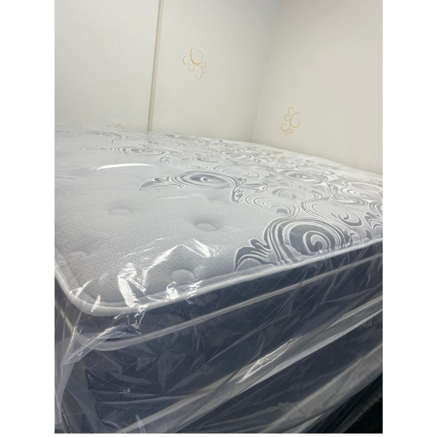 Vivians 13" Innerspring Mattress With Gray Quilt, Inside Of A Showroom, Stacked On Top Of Other Mattresses, Zoomed In