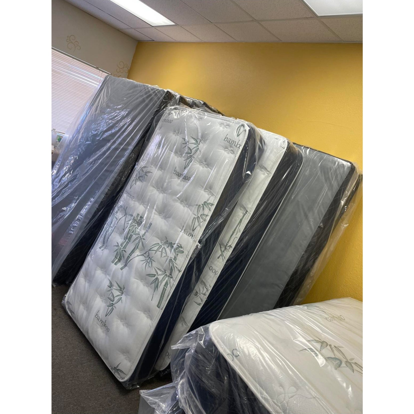 Vivians 8.5" Innerspring Mattress With White Bamboo Quilt, Inside Of A Showroom, Stacked Upright Against Other Mattresses